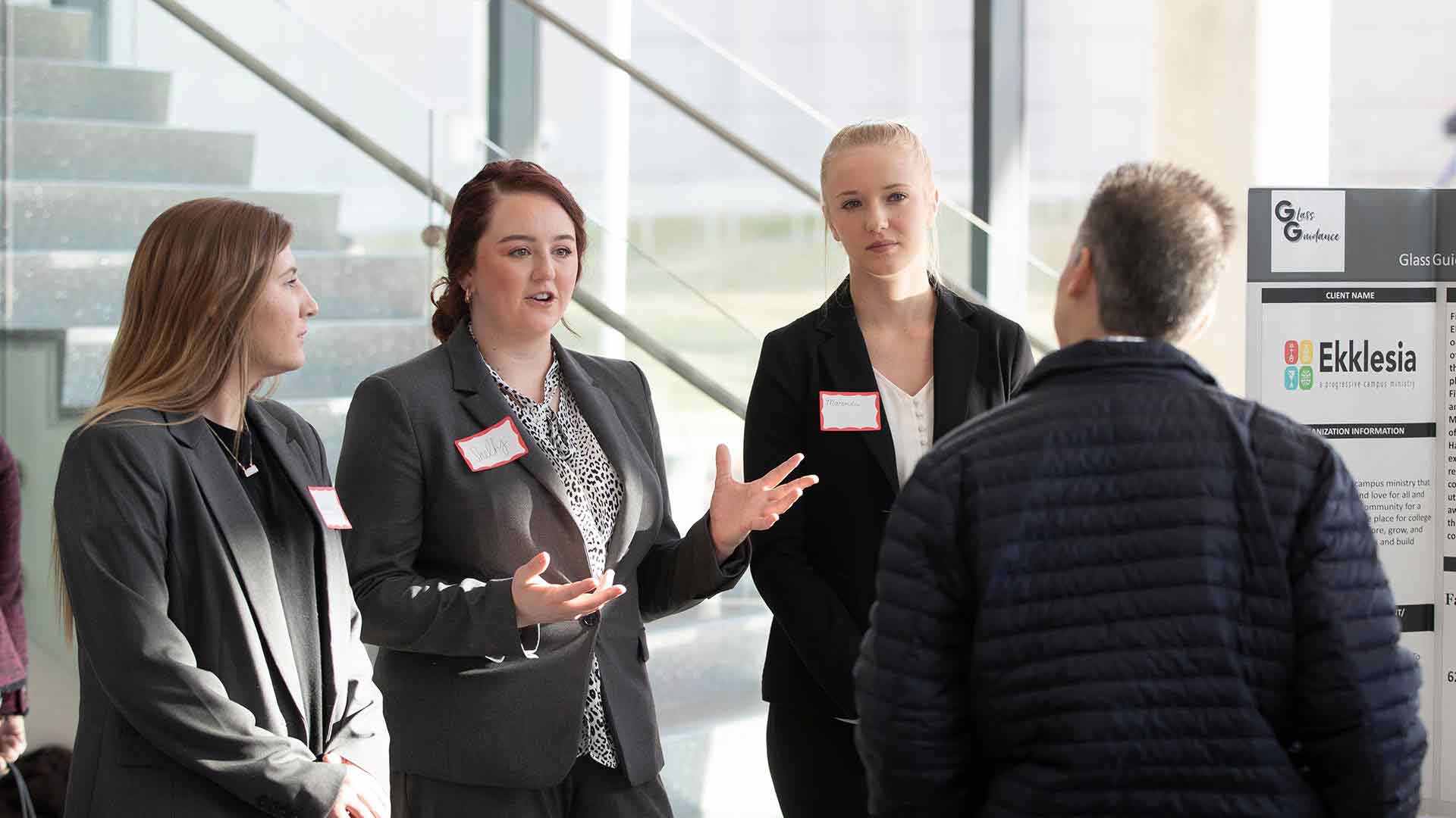 Management students presenting at symposium in Glass Hall atrium