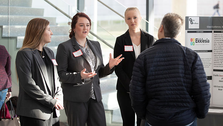 Management students presenting at symposium in Glass Hall atrium